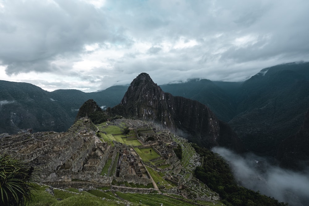 green grass field near mountain under cloudy sky during daytime