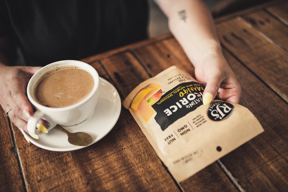 person holding white ceramic cup with brown liquid inside