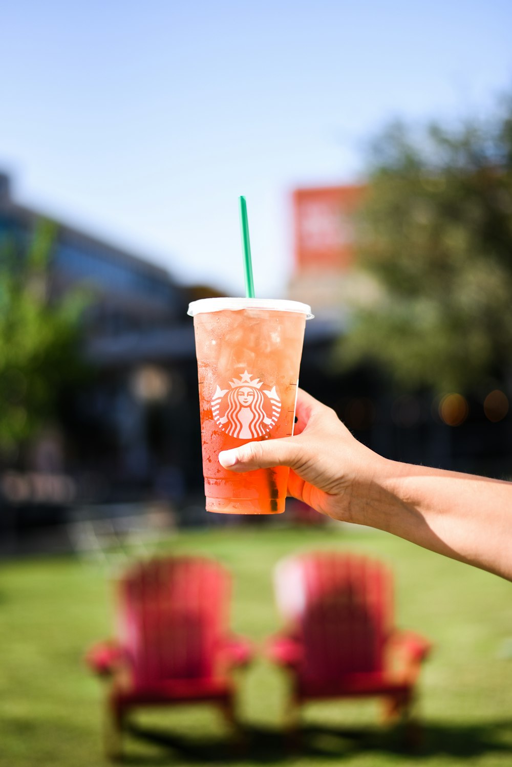 Persona sosteniendo un vaso de plástico naranja y blanco con pajita verde