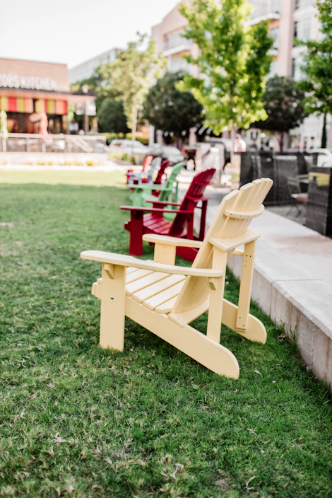 A colorful plastic Adirondack chair set outdoors on a sunny patio surrounded by greenery.