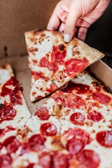 Close-up of a hand picking up a pizza box from a black counter with red accents in a cozy pizzeria.