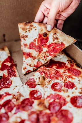 Close-up of a hand holding a phone with a delicious pizza box in the background.