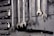 A collection of open-end and box-end wrenches hang on a weathered wooden board. The metal tools are neatly organized in a row, displaying their shiny metallic surfaces. A black hose or pipe with fittings is also visible below the wrenches.