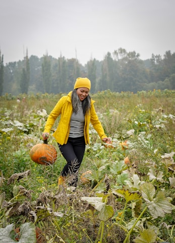 woman in yellow jacket and black pants sitting on pumpkin during daytime