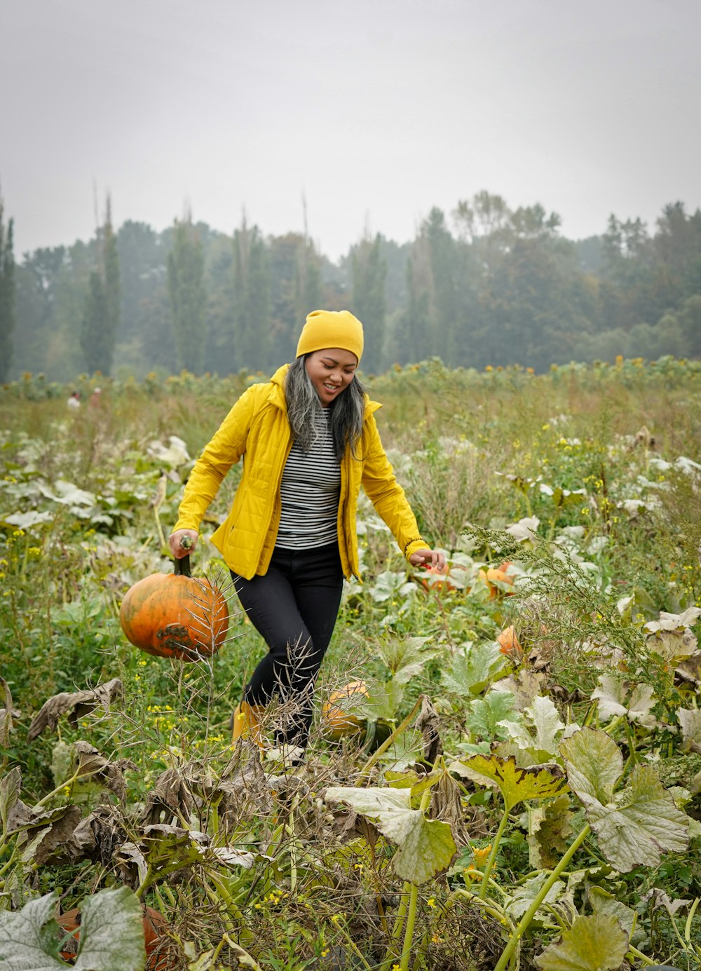 woman in yellow jacket and black pants sitting on pumpkin during daytime
