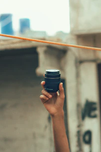 Close-up of a hand holding a compact pepper spray canister against a blurred urban background.