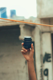 Close-up of a hand holding a compact pepper spray canister against a blurred urban background.