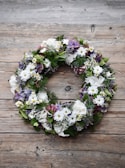 Elegant funeral wreath with white lilies and greenery on a wooden stand.