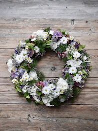 A delicate handmade wreath featuring soft purple and teal flowers with subtle silver accents.