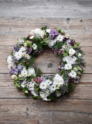 Elegant funeral wreath with white lilies and greenery on a wooden stand.