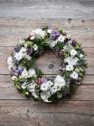 A serene funeral wreath arrangement with soft white and green flowers placed respectfully on a wooden table.