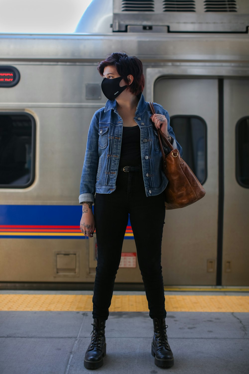 woman in blue denim jacket and black pants standing beside train