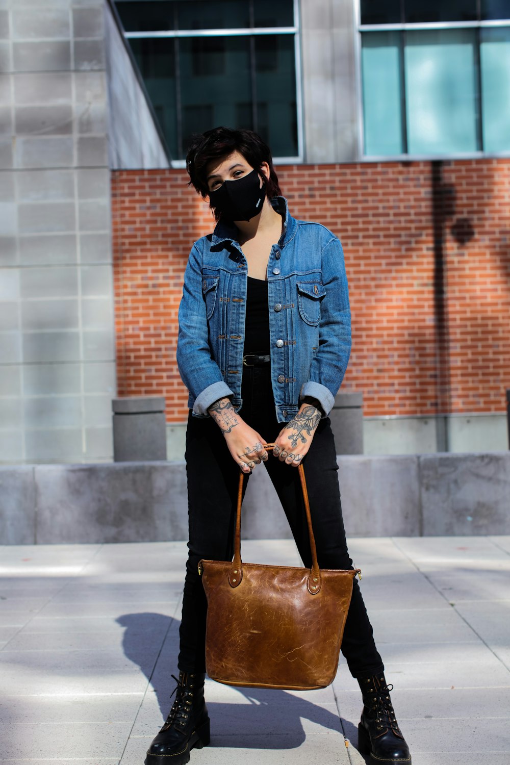 woman in blue denim jacket and black pants holding brown leather handbag