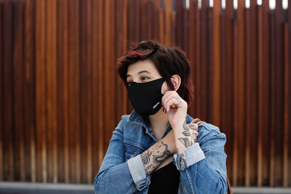 woman in blue denim jacket covering face with black mask