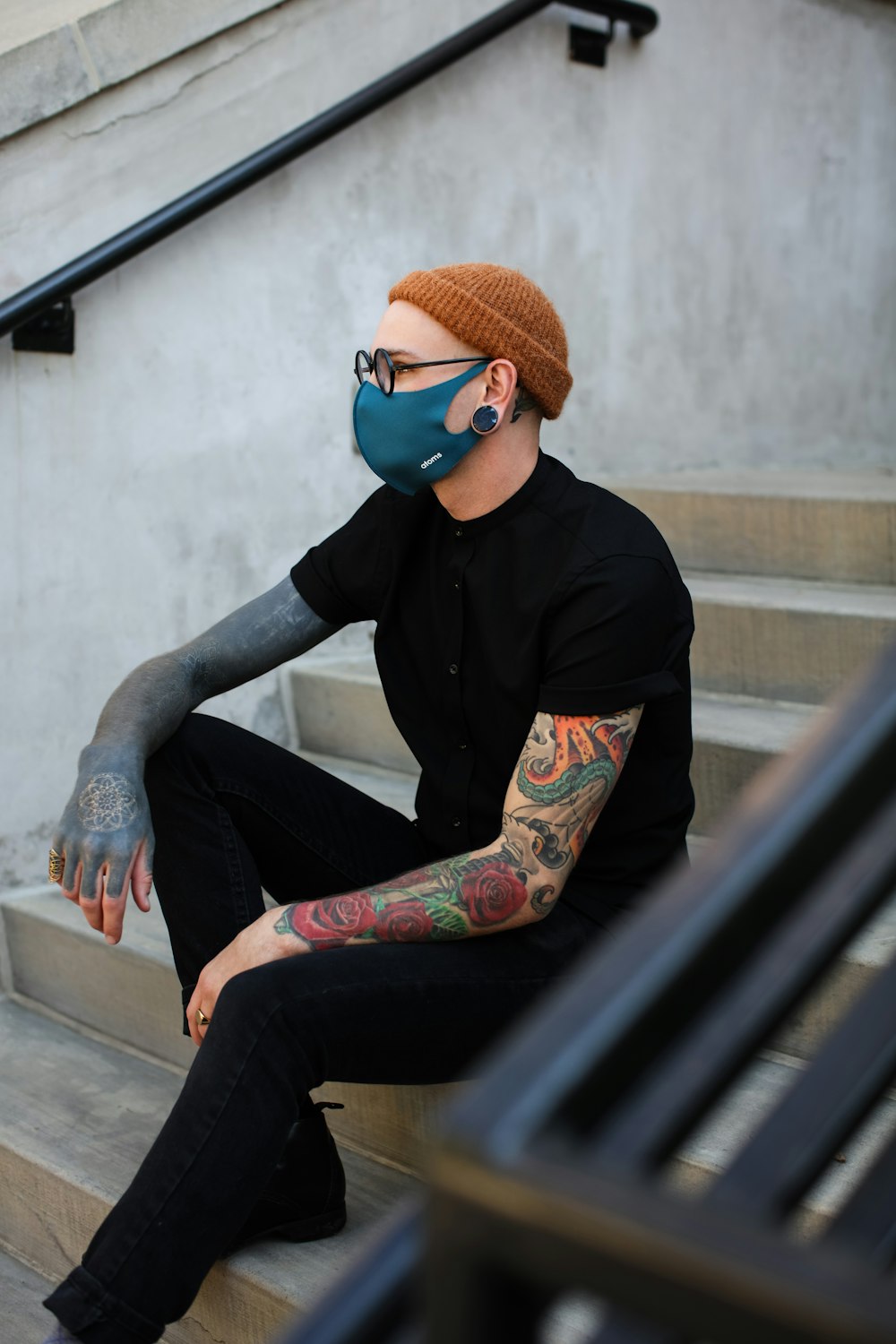 man in black jacket and blue denim jeans sitting on black metal bench