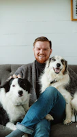 man in gray sweater sitting beside black and white border collie