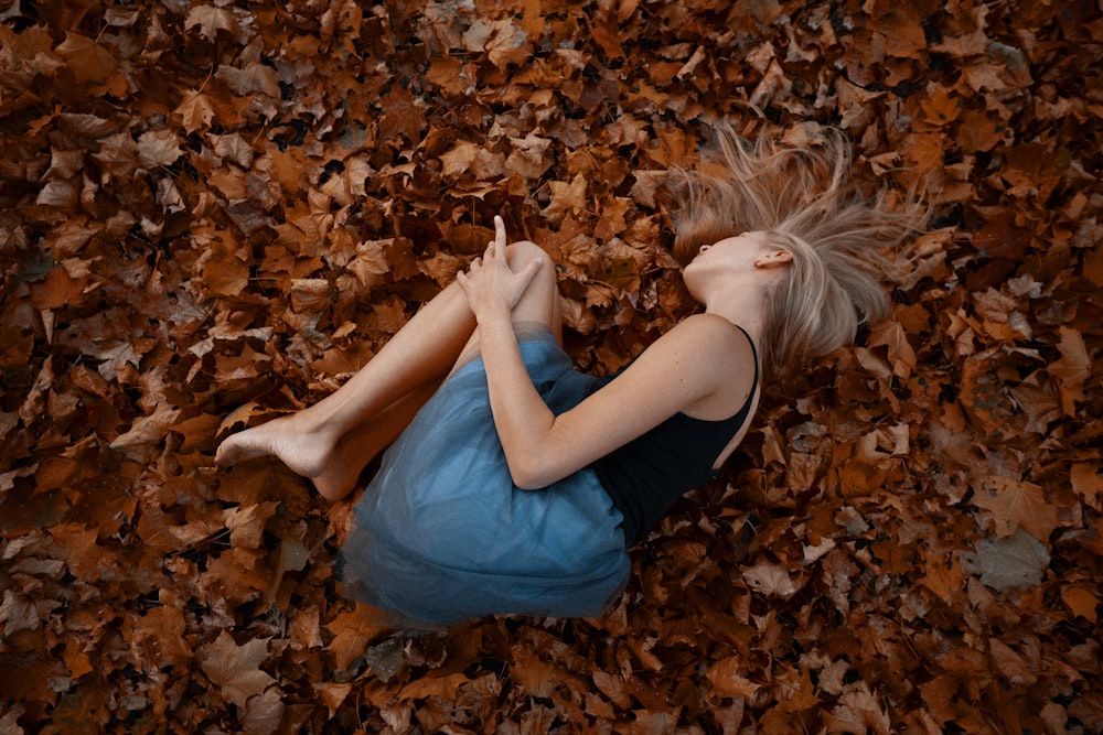 woman in blue tank top lying on dried leaves