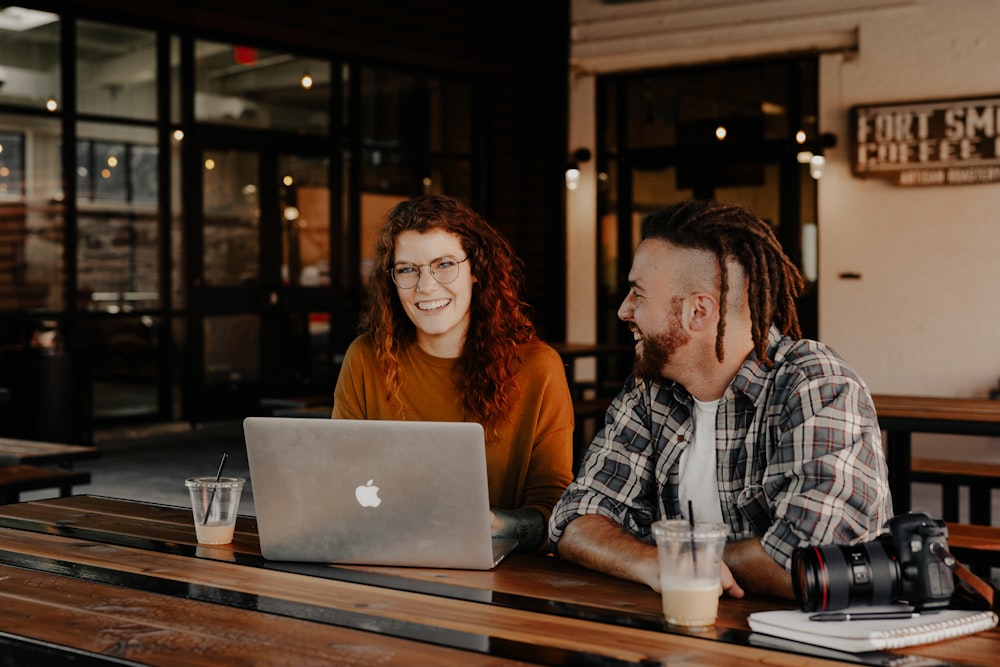 Homem e mulher sentados na frente do MacBook prateado