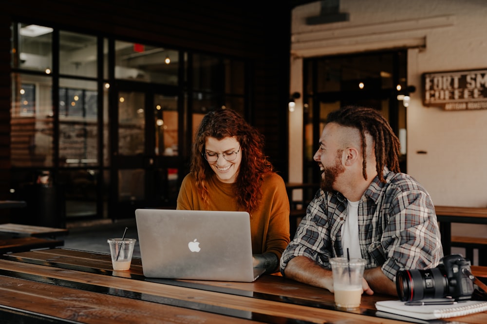 man and woman sitting at table using macbook