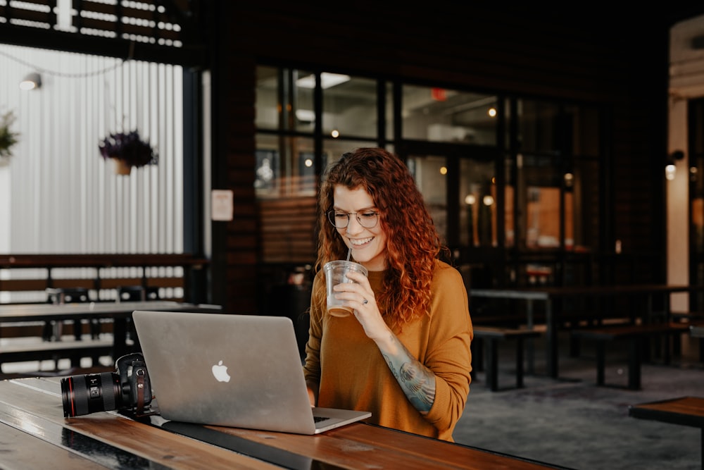 woman in brown long sleeve shirt sitting by the table using macbook