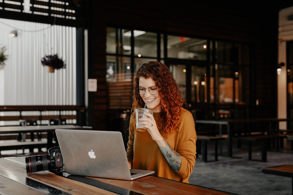 Donna in camicia a maniche lunghe marrone che si siede vicino al tavolo usando MacBook
