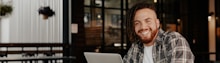 man in black and white plaid dress shirt sitting by the table using macbook