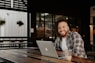 man in black and white plaid dress shirt sitting by the table using macbook