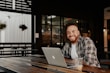 man in black and white plaid dress shirt sitting by the table using macbook