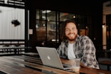 man in black and white plaid dress shirt sitting beside table with macbook