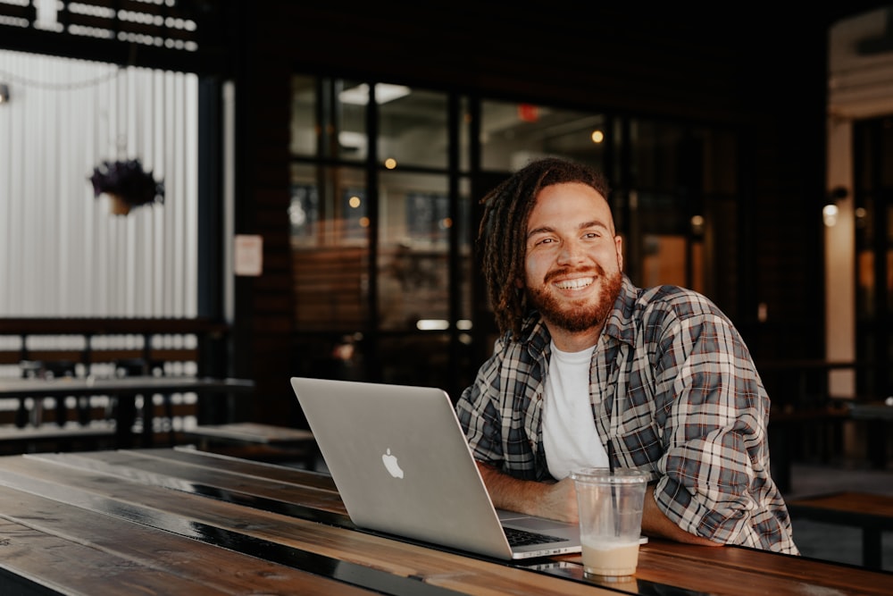 man in black and white plaid dress shirt sitting beside table with macbook