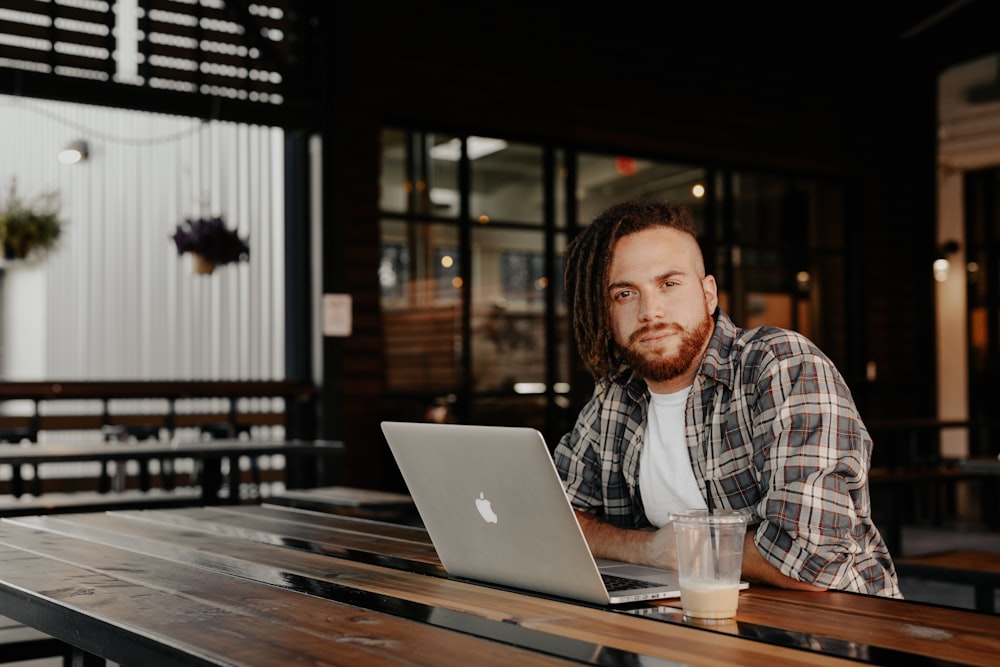 man in black and white plaid dress shirt sitting by the table using macbook