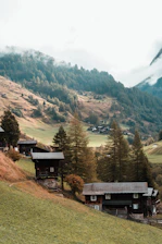 A serene luxury farmhouse nestled among pine trees with misty Himalayan peaks in the background at sunrise.