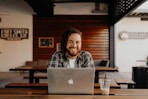 man in black and white striped polo shirt sitting on chair in front of silver macbook