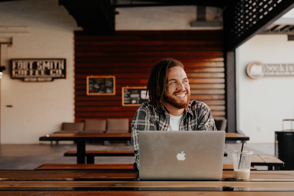 Hombre en camisa de vestir a cuadros blanco y negro sentado frente a Macbook plateado