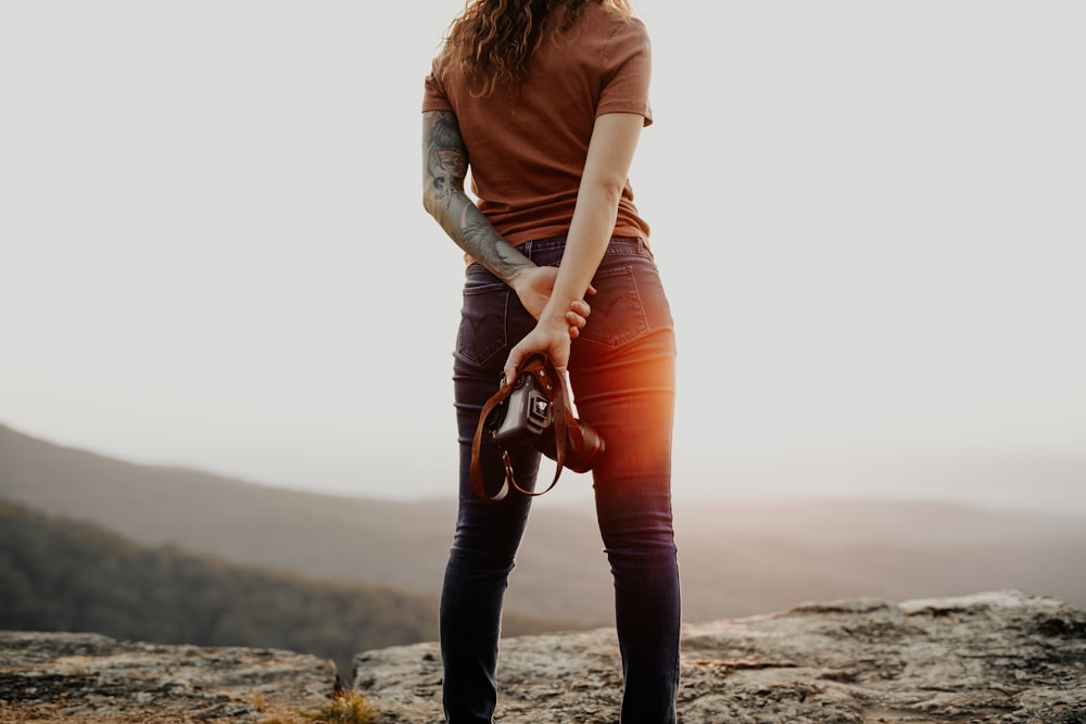 Femme en chemise à manches longues marron et jean en denim bleu tenant un sac en cuir marron