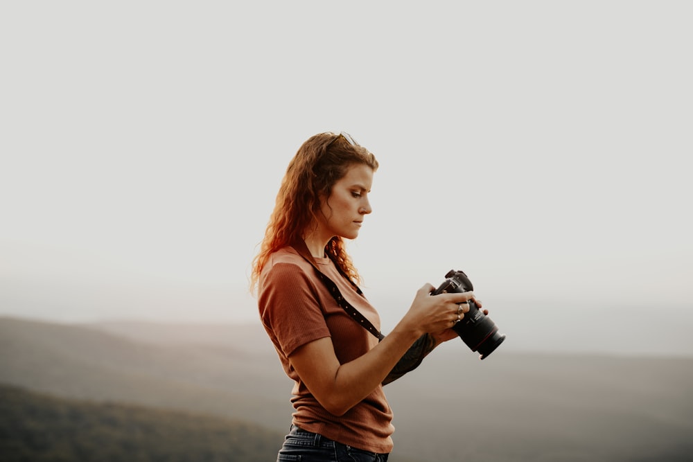 woman in orange shirt and blue denim shorts holding black dslr camera