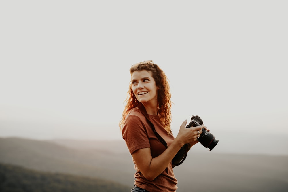 mujer con camisa naranja sosteniendo una cámara réflex digital negra