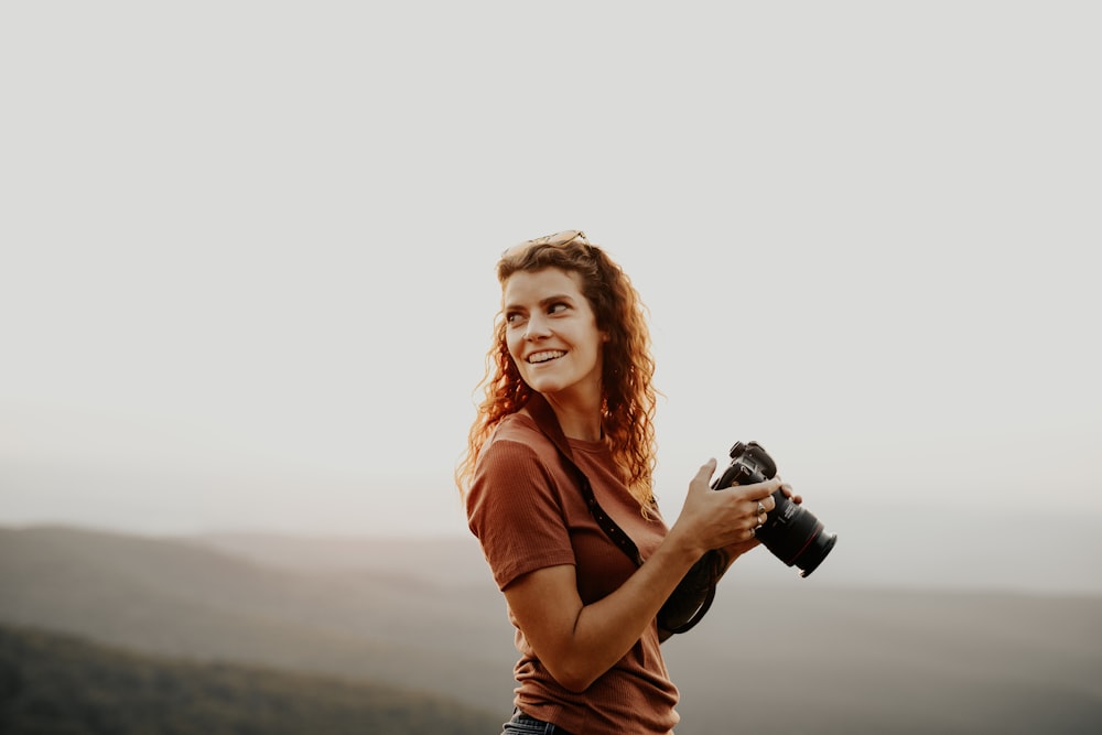 Frau in orangefarbenem Hemd mit schwarzer DSLR-Kamera