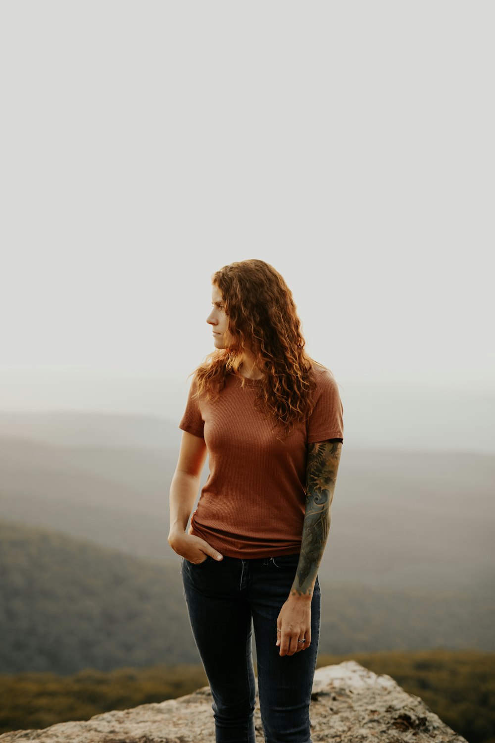 woman in brown tank top and blue denim jeans standing on seashore during daytime