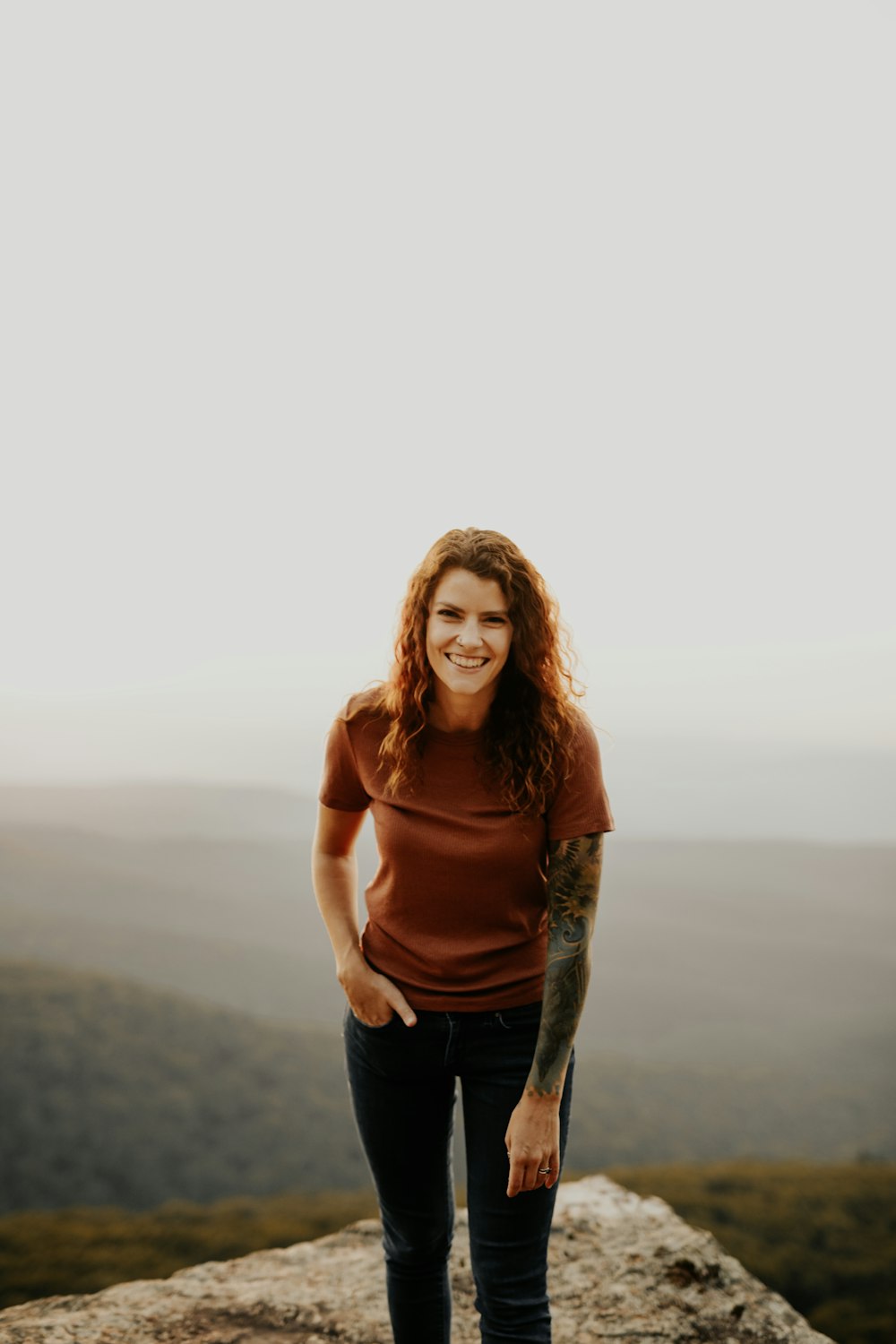 woman in brown long sleeve shirt and blue denim jeans standing on brown field during daytime