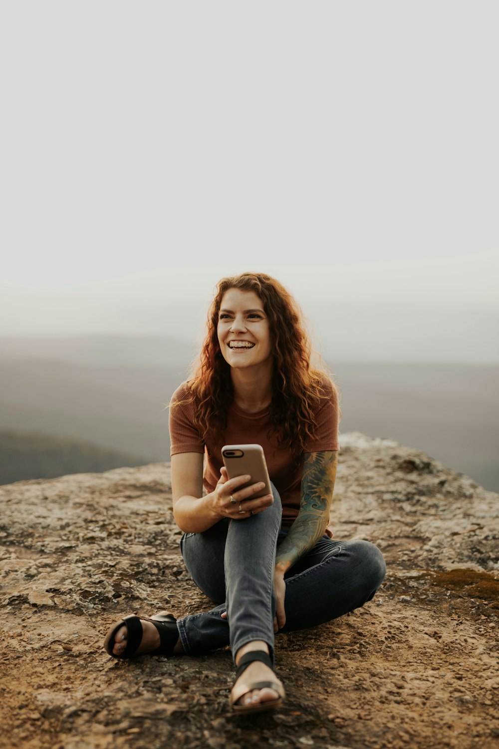 Femme en chemise à manches longues marron et jean en denim bleu assise sur un rocher