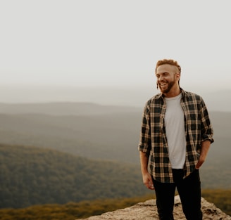 man in brown and white plaid button up shirt standing on brown rock during daytime