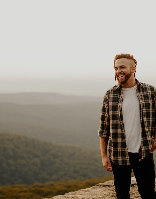 man in brown and white plaid button up shirt standing on brown rock during daytime