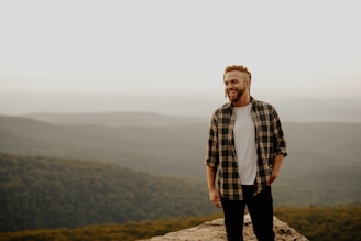 man in brown and white plaid button up shirt standing on brown rock during daytime