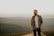 man in brown and white plaid button up shirt standing on brown rock during daytime