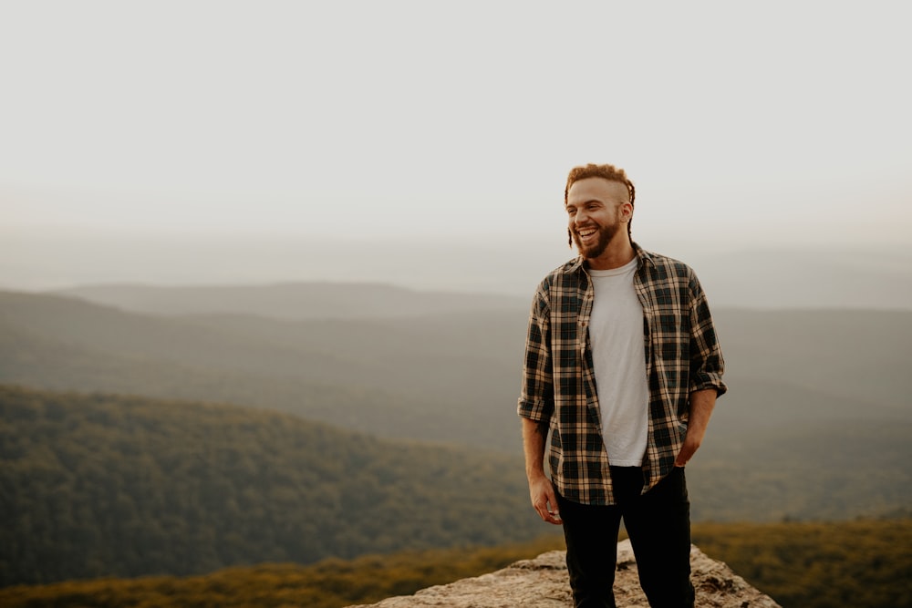 man in brown and white plaid button up shirt standing on brown rock during daytime