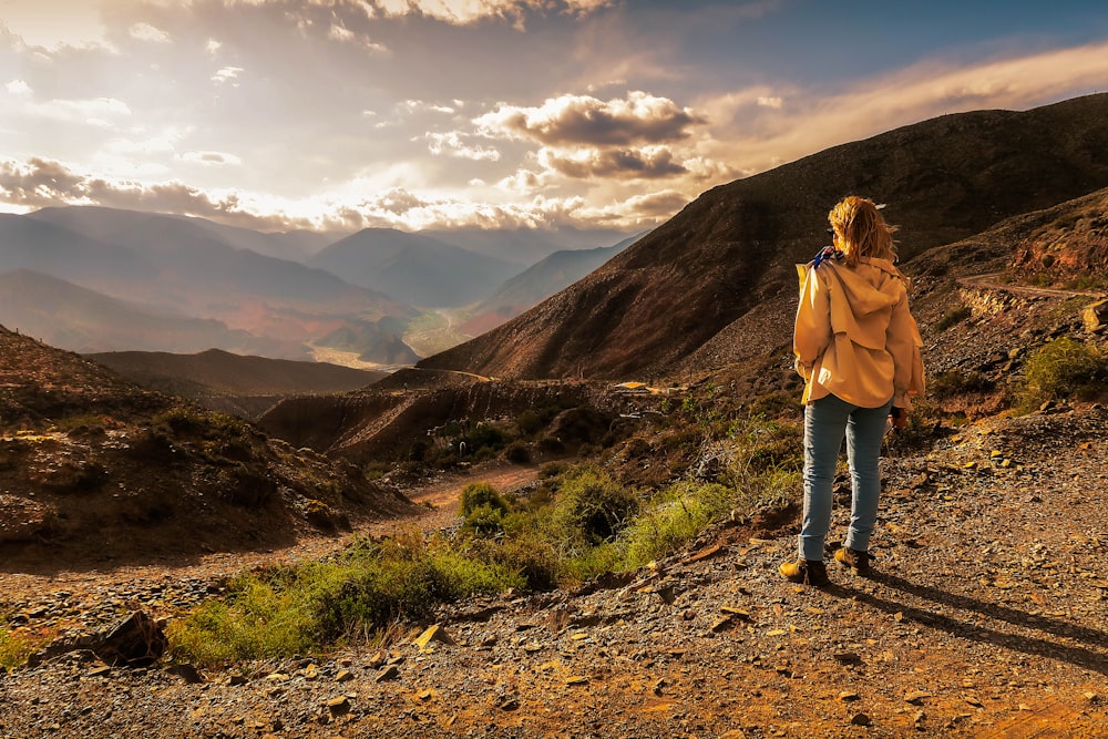 woman in beige jacket standing on brown dirt road during daytime