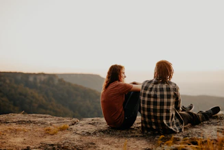 woman in black and white plaid shirt sitting on brown rock during daytime