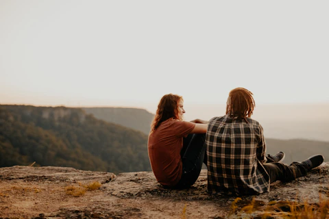 woman in black and white plaid shirt sitting on brown rock during daytime