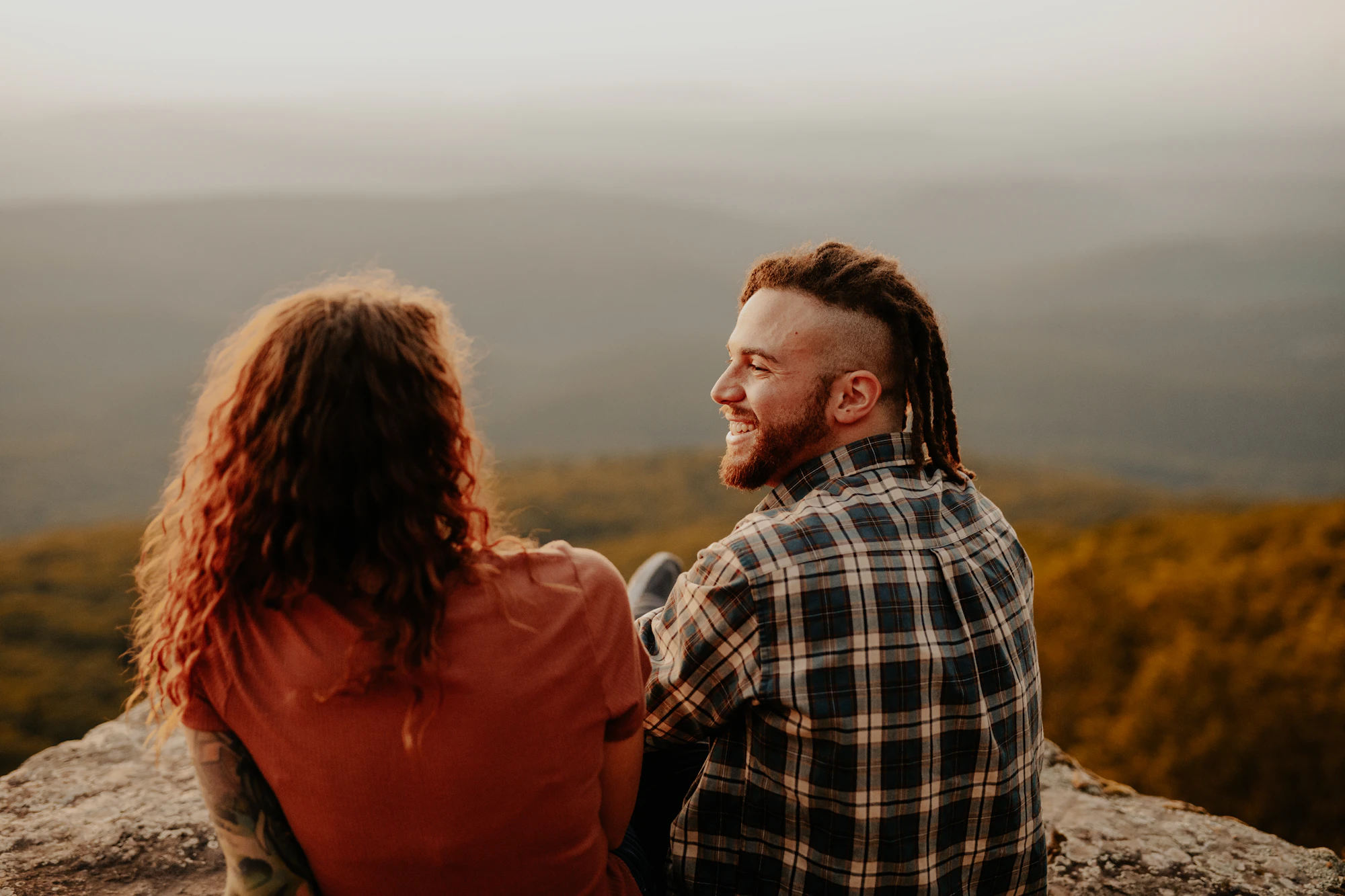 Nora and Jalen standing close in a golden field with mountains behind them